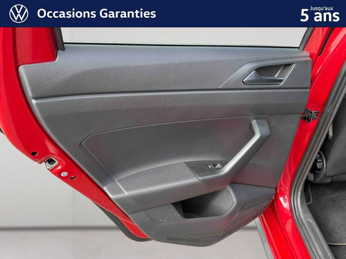 Vue rapprochée de la porte arrière gauche rouge métallisée d'une Volkswagen Polo 2025 avec garniture intérieure noire.