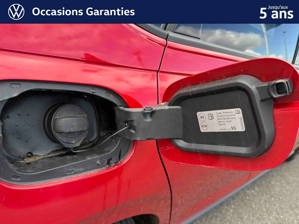 Gros plan sur la trappe à carburant ouverte côté gauche d'une Volkswagen Polo rouge métallisée.