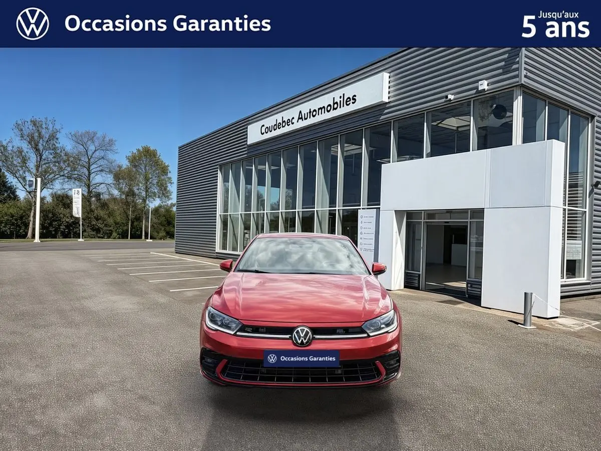 Vue avant d'une Volkswagen Polo rouge métallisée garée devant un bâtiment moderne de concession automobile.