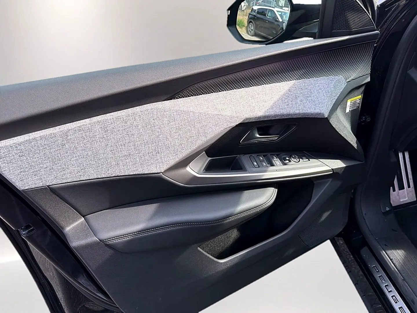 Vue intérieure côté gauche de la porte avant noire du Peugeot 5008 Hybrid 145 GT avec habillage tissu gris et commandes électriques.