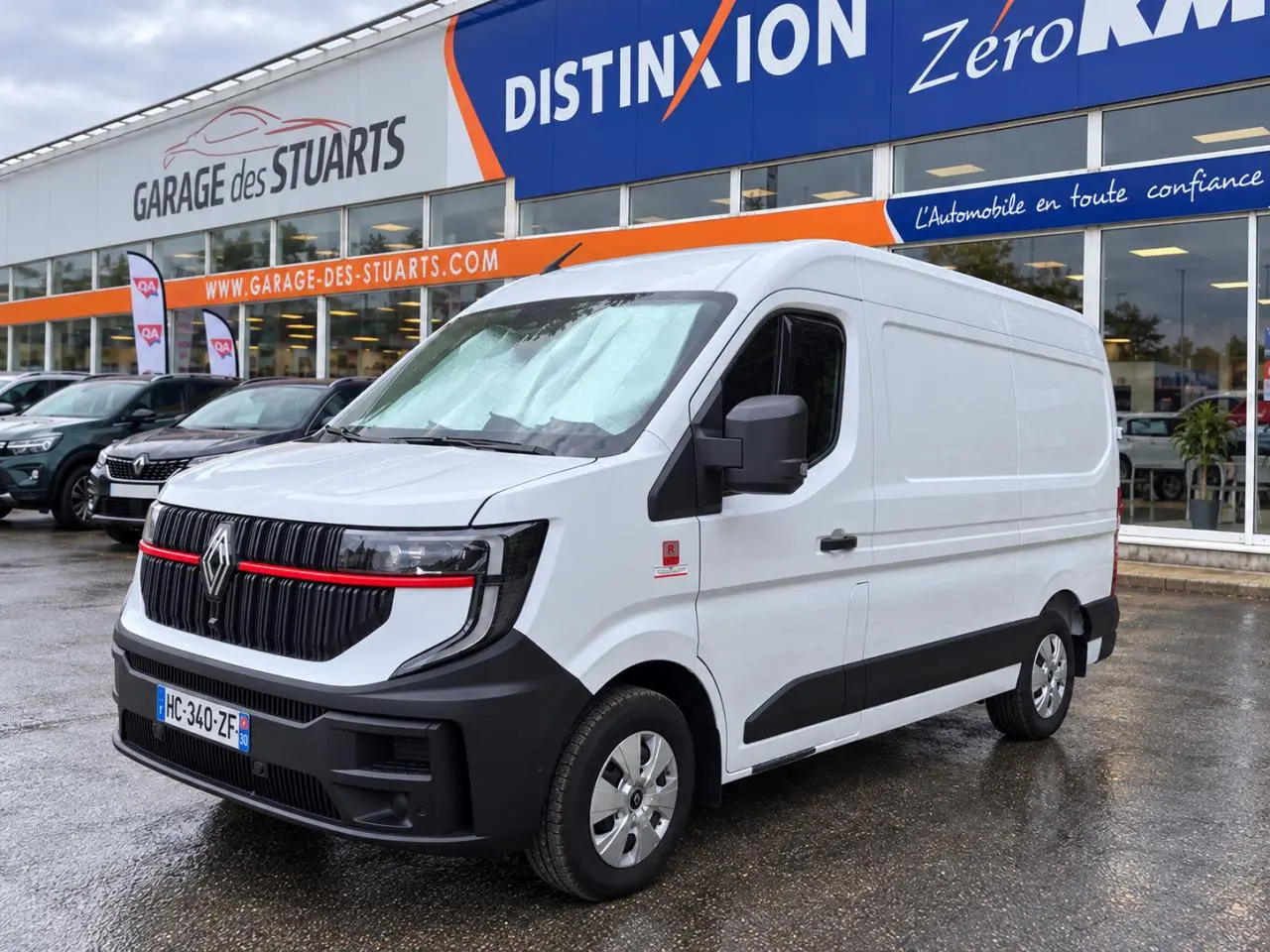 Renault Master blanc en 3/4 avant droit, fourgon L2H2 avec calandre noire et bande rouge distinctive.