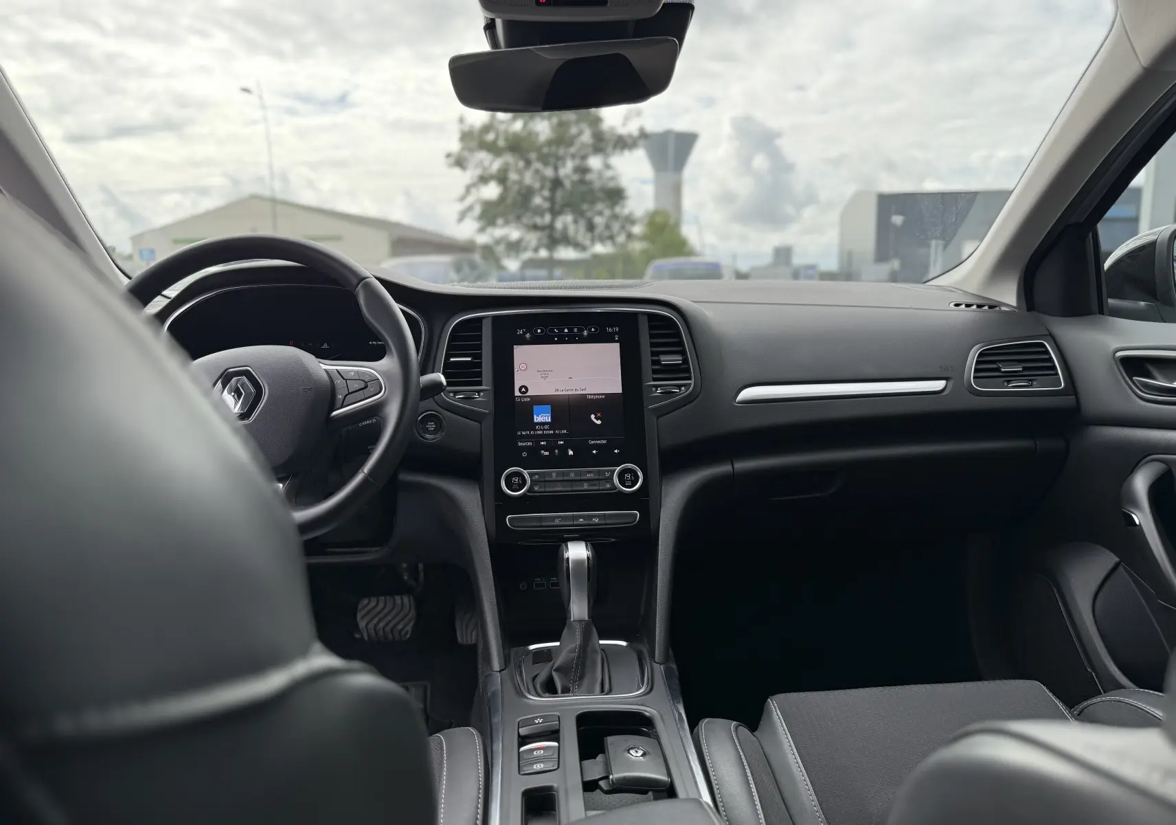 Vue intérieure avant de la Renault Mégane Break 2024, tableau de bord moderne avec écran tactile et volant multifonction noir.