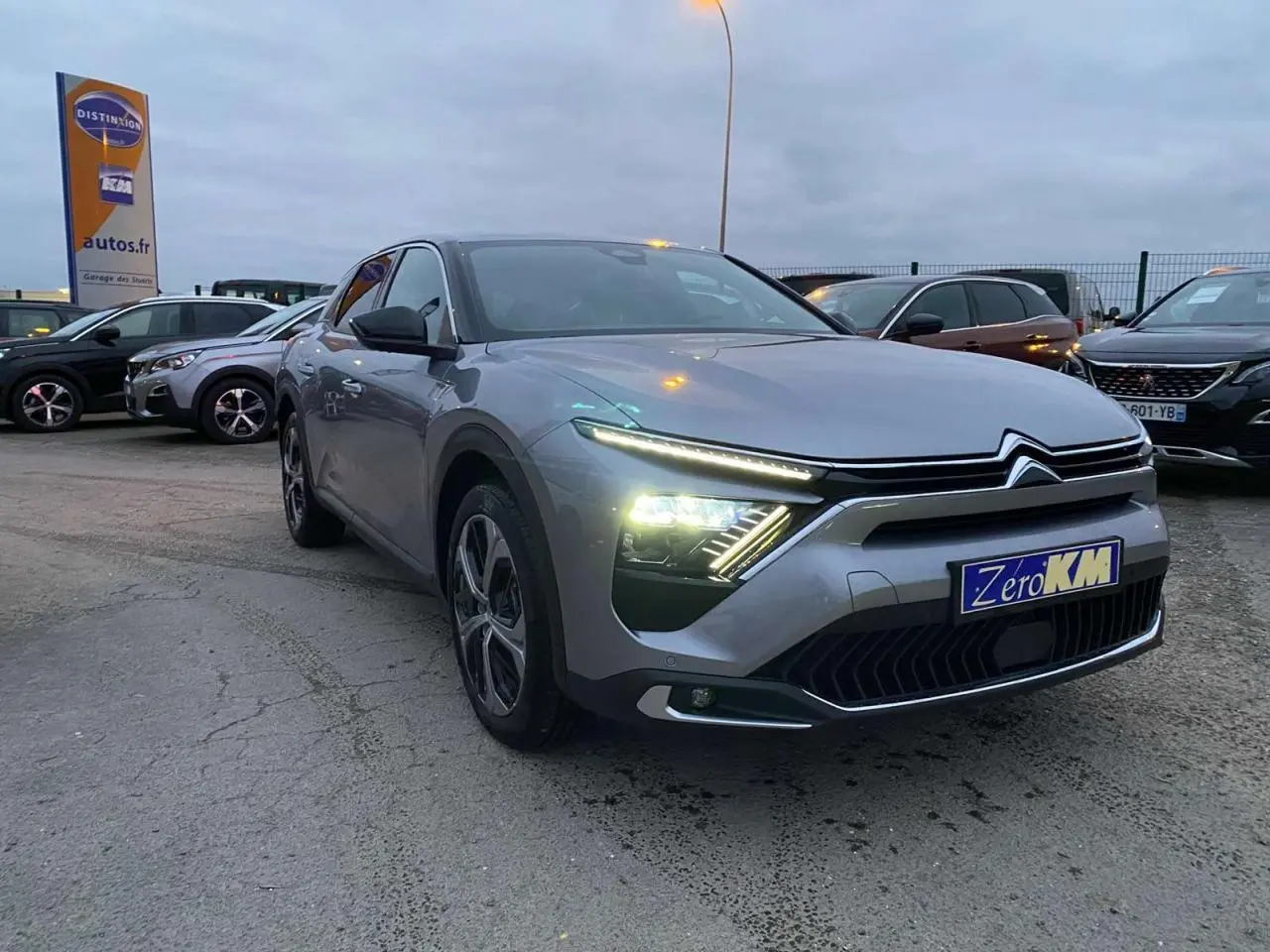 Citroën C5 X gris Artense métal en 3/4 avant droit avec phares LED allumés sur parking extérieur.