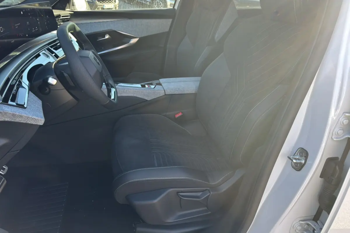 Vue intérieure côté conducteur du Peugeot 3008 Hybrid 2024 blanc okénite, avec sièges en tissu et alcantara noirs et tableau de bord moderne.