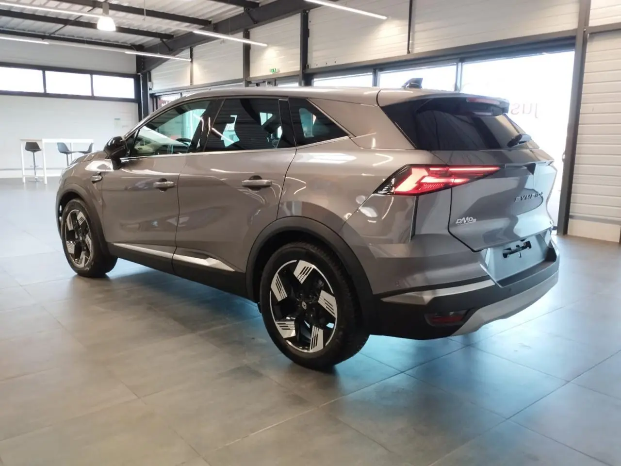 Vue 3/4 arrière droite du Renault SYMBIOZ gris Cassiopée avec jantes 18 pouces et feux arrière LED allumés.