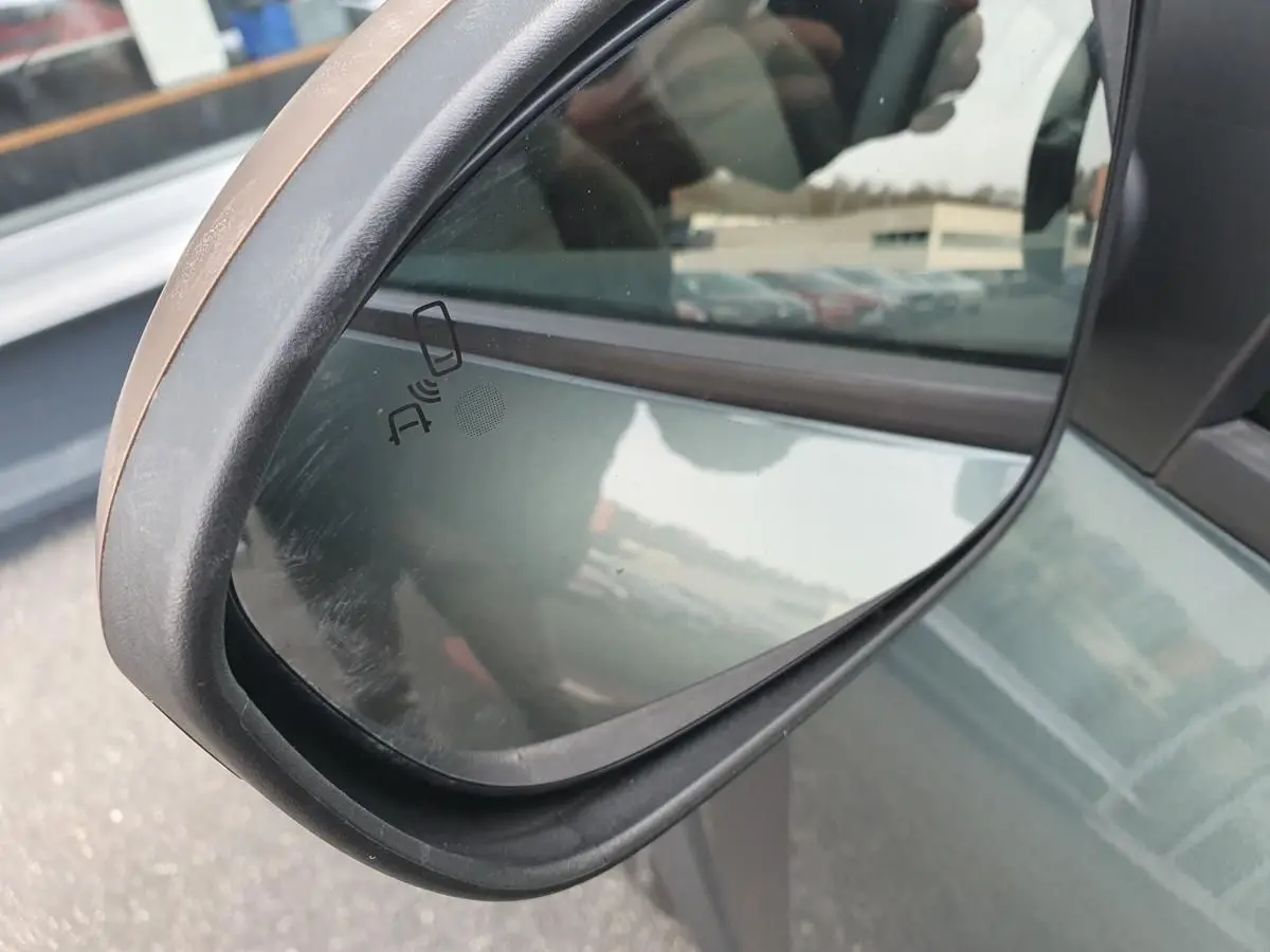 Rétroviseur côté gauche du Dacia Jogger vert cèdre 2026 avec signalisation d'alerte d'angle mort visible.