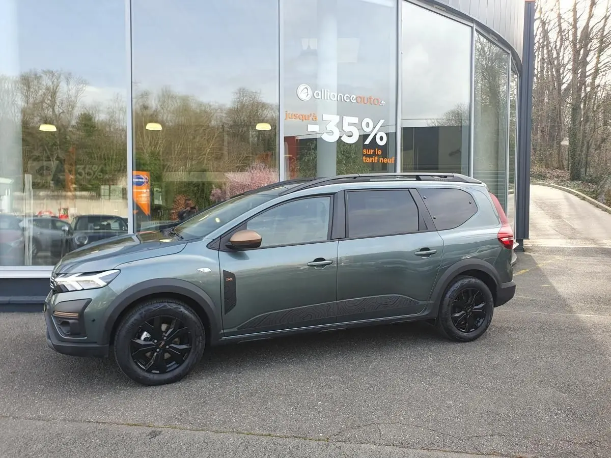 Vue de profil côté gauche d'un Dacia Jogger vert cèdre avec jantes noires et barres de toit longitudinales.