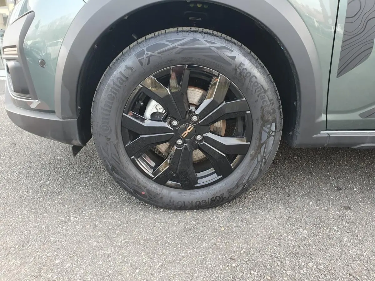 Gros plan sur la roue avant droite noire avec jante aluminium 16” Mahalia du Dacia Jogger vert cèdre.