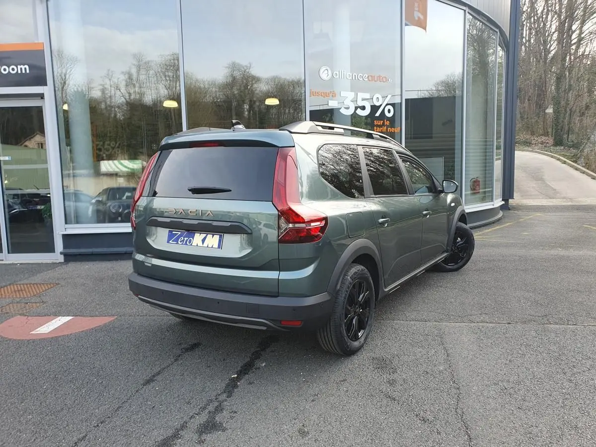 Vue 3/4 arrière droite d'un Dacia Jogger vert cèdre avec jantes noires et barres de toit modulaires.