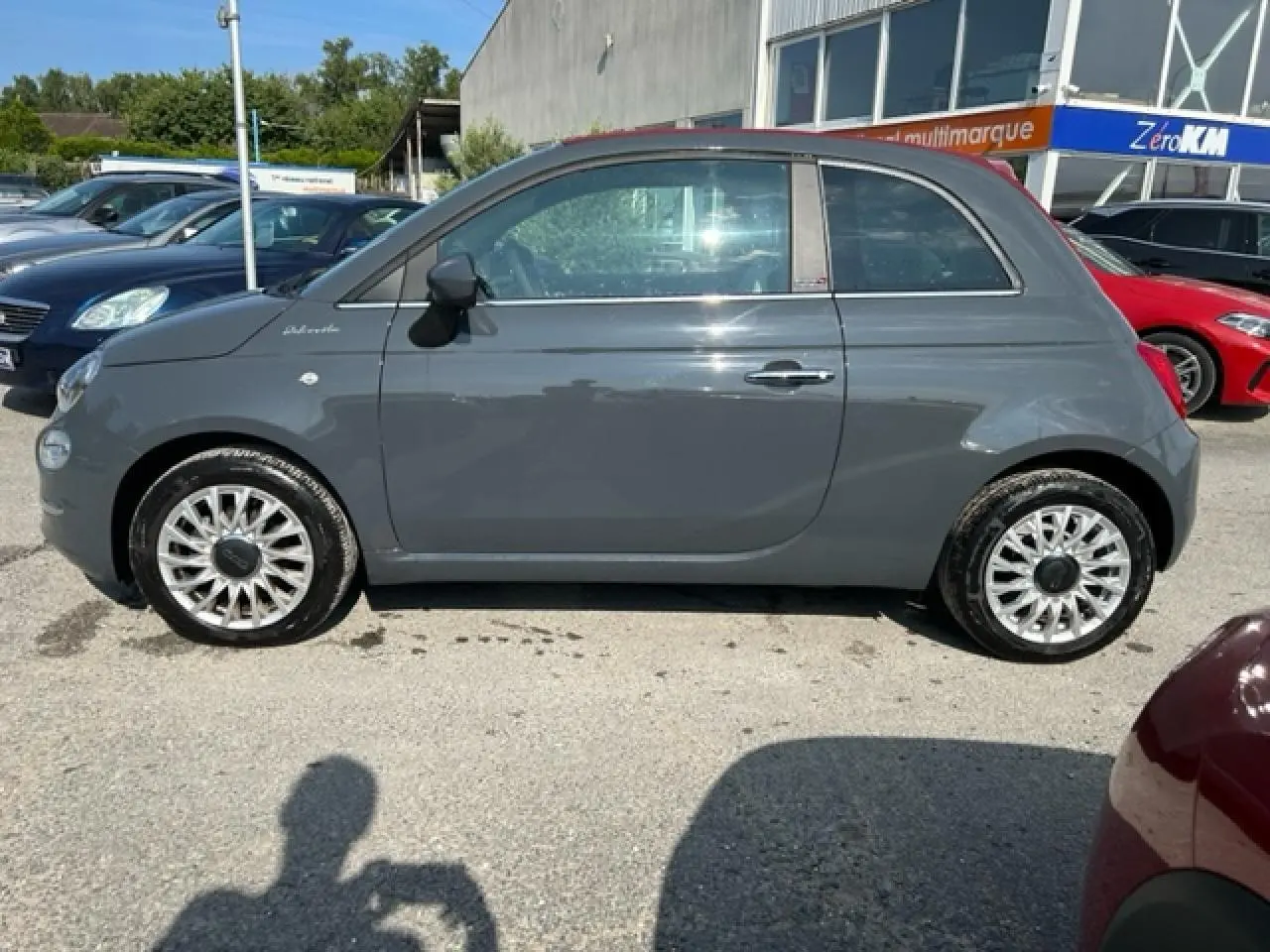 Vue de profil côté gauche d'une FIAT 500C cabriolet 2021 gris avec capote rouge fermée et jantes argentées.