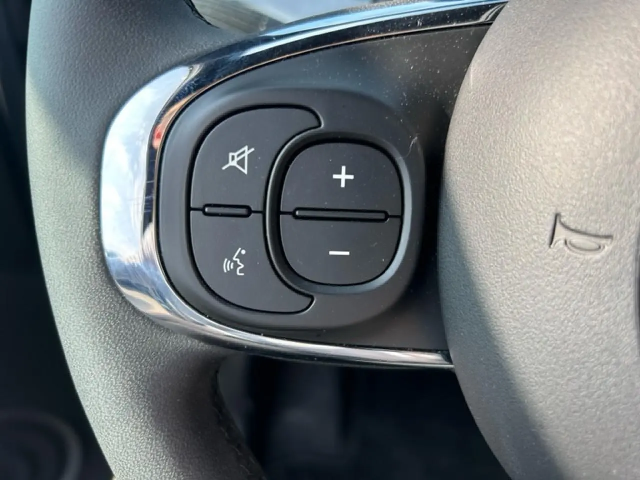 Gros plan sur les commandes de volume et de coupure du son au volant de la Fiat 500C Dolcevita gris et rouge.
