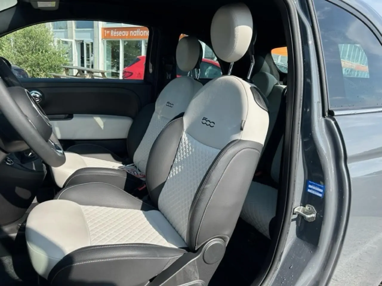 Vue intérieure côté conducteur de la FIAT 500C gris avec sellerie bicolore beige et noire au design matelassé.