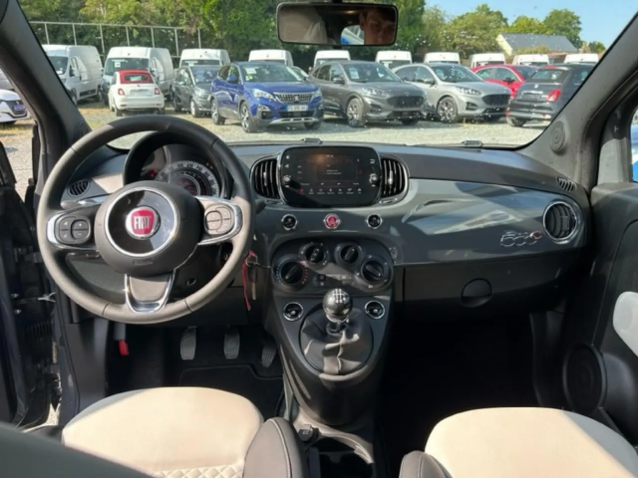 Vue intérieure avant de la Fiat 500C gris et rouge, avec tableau de bord brillant et volant multifonction noir.