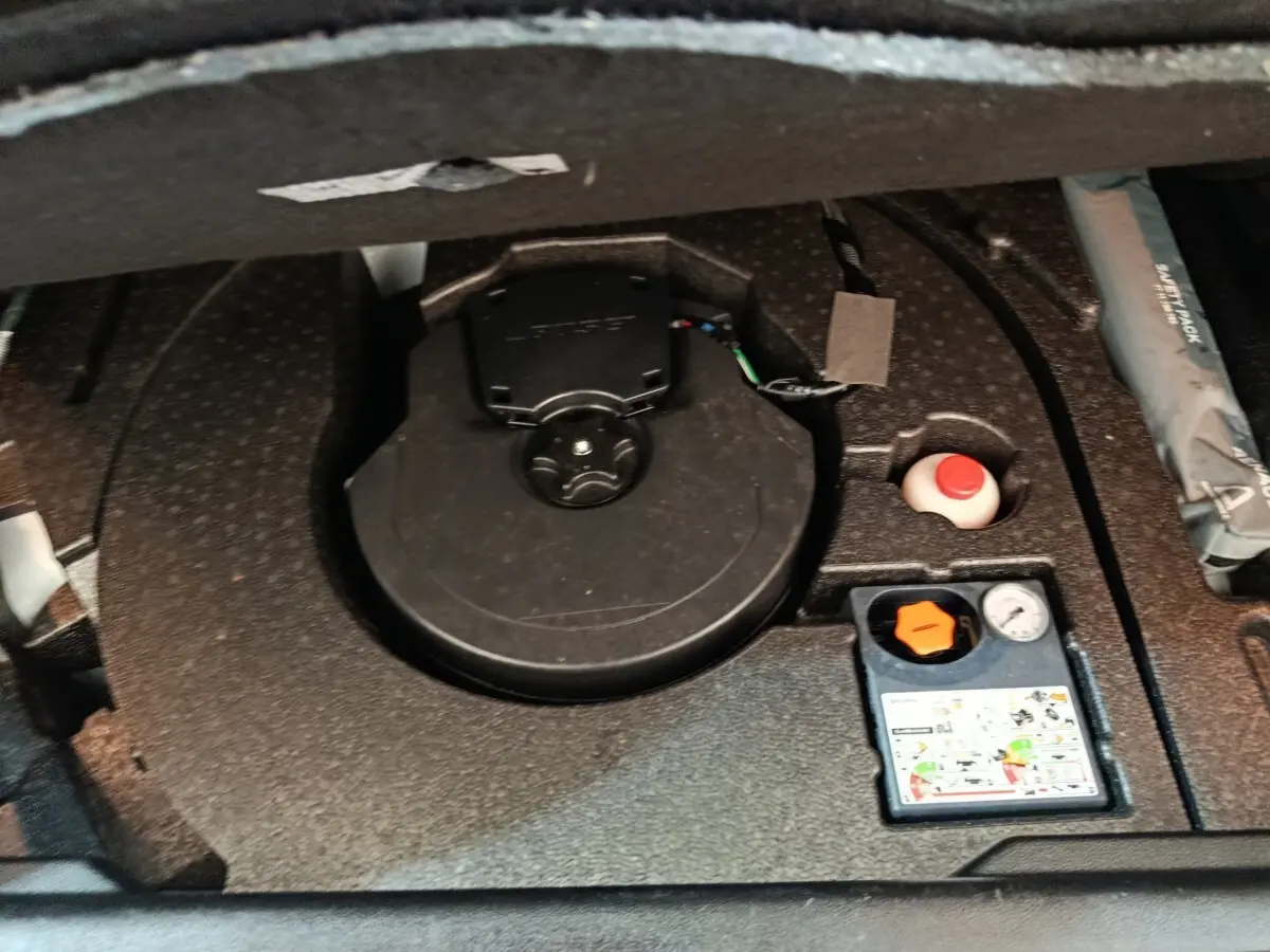 Vue rapprochée du coffre du Renault Kadjar blanc, montrant le logement de la roue de secours et les accessoires de gonflage.