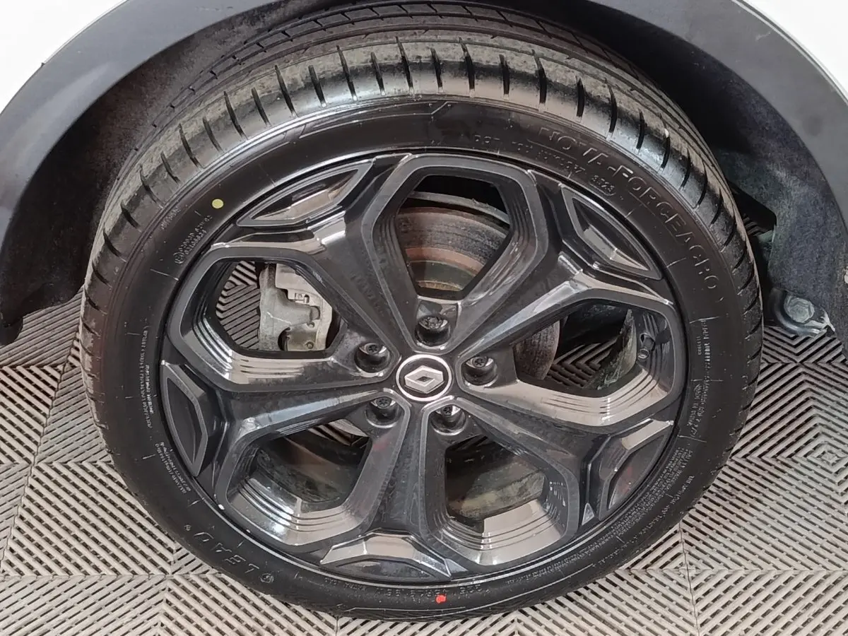 Gros plan sur la roue arrière droite noire d’un Renault Kadjar blanc, avec jante et pneu visibles sur sol texturé.