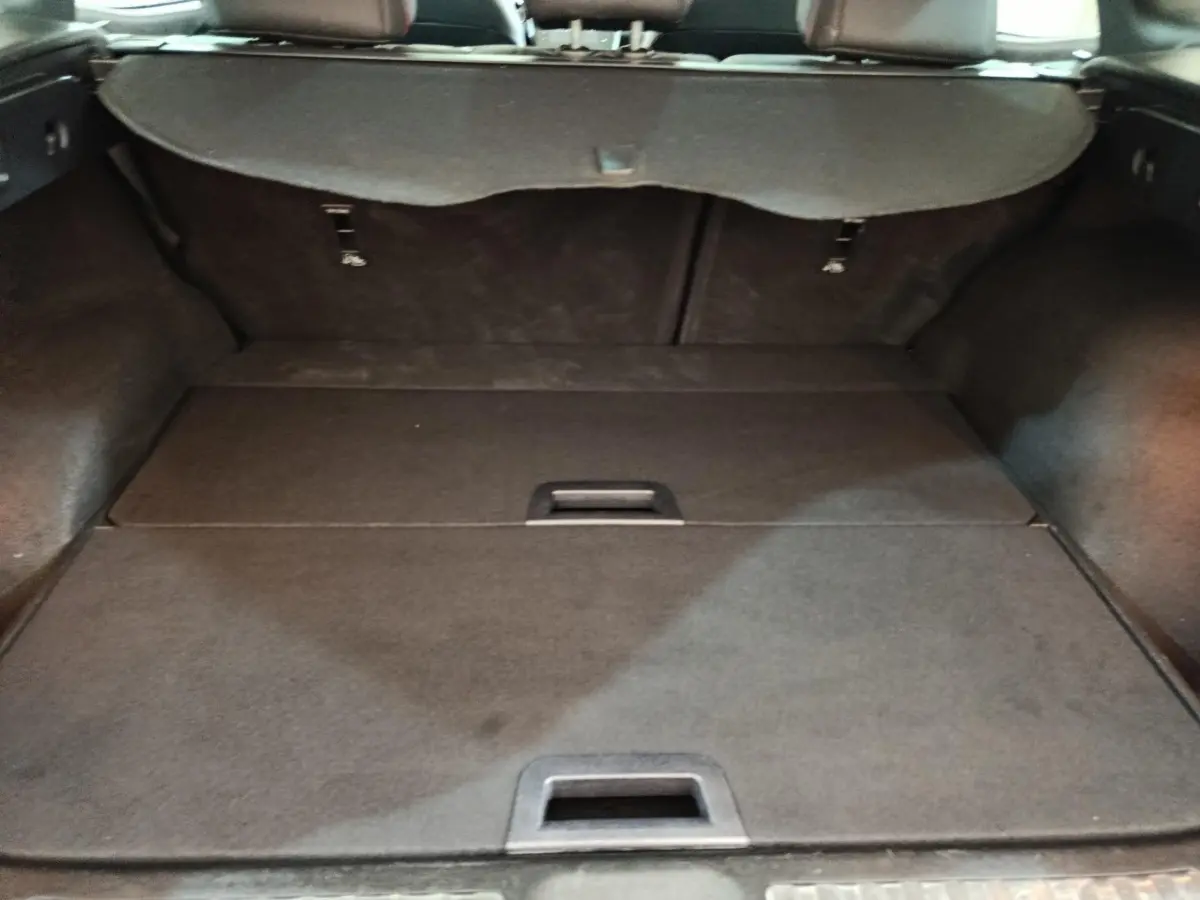 Coffre ouvert vu de l'intérieur d'un Renault Kadjar blanc, avec banquette arrière rabattue et cache-bagages en place.