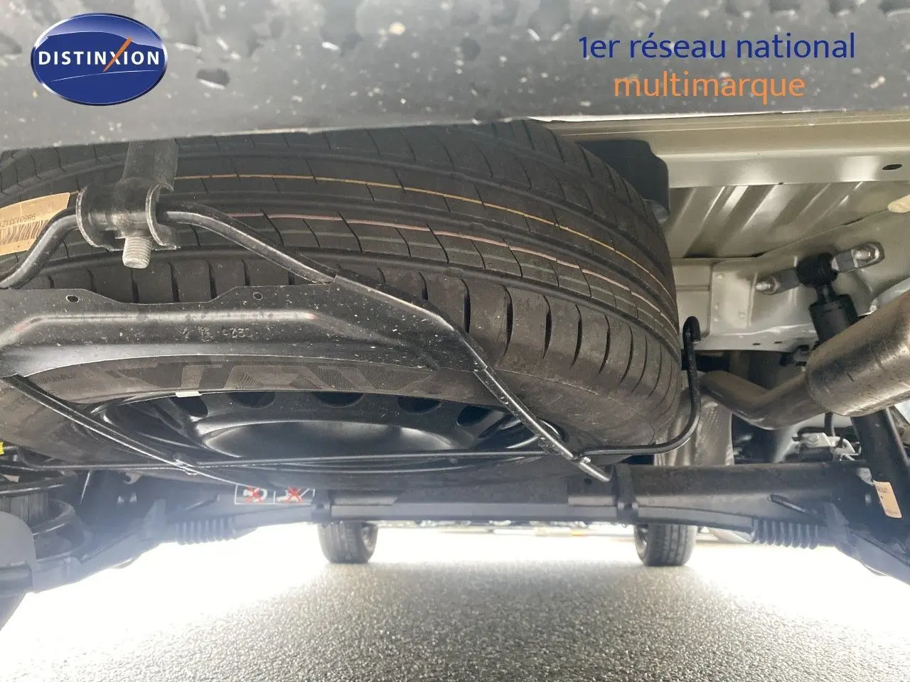 Vue en contre-plongée sous le Citroën Berlingo Fourgon blanc, montrant la roue de secours et le système de suspension arrière.
