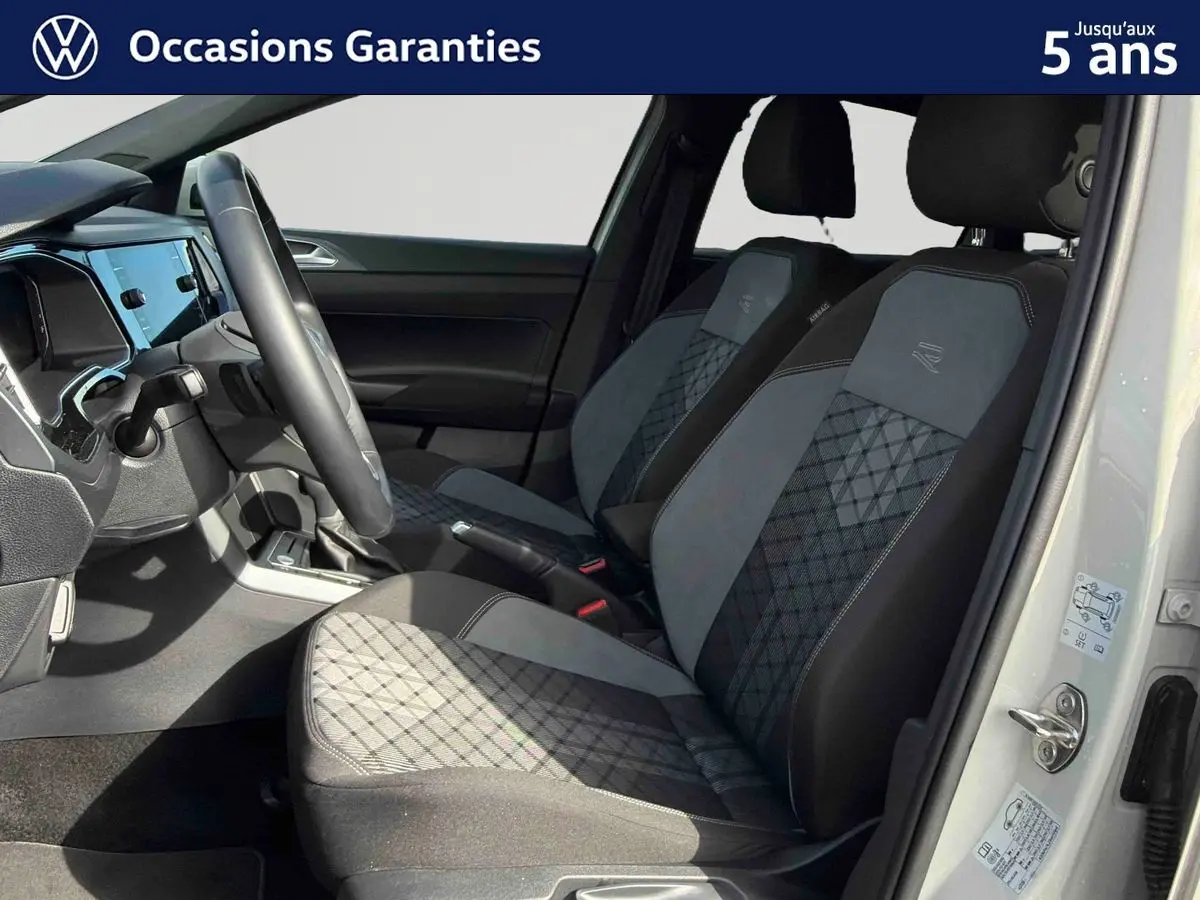 Vue intérieure côté conducteur du Volkswagen Taigo gris, mettant en valeur les sièges sport-confort à motifs géométriques et le volant multifonctions.