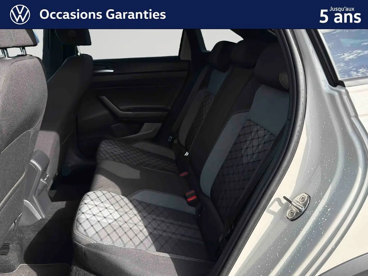 Vue intérieure côté droit des sièges arrière gris à motifs du Volkswagen Taigo 2025 avec porte ouverte et carrosserie grise visible.