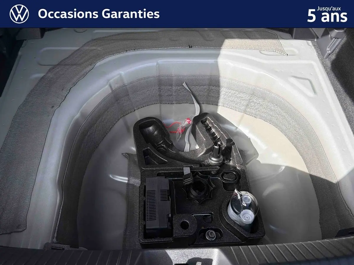 Vue plongeante sur le coffre ouvert d’un Volkswagen Taigo gris, montrant le rangement sous plancher avec attelage amovible.