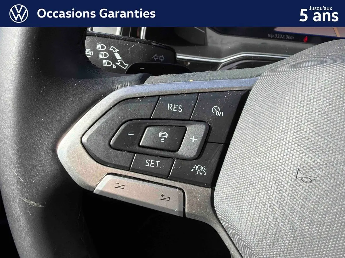 Gros plan sur les commandes du volant gris du Volkswagen Taigo 2025, avec boutons de régulateur de vitesse et assistance conduite.