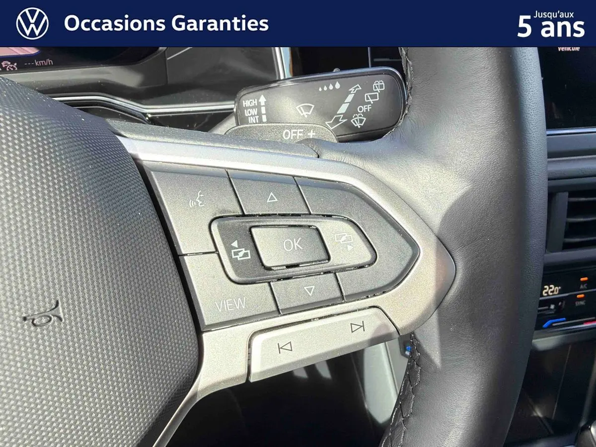 Gros plan sur les commandes multifonctions gauche du volant cuir du Volkswagen Taigo gris, avec tableau de bord et climatisation tactile en arrière-plan.