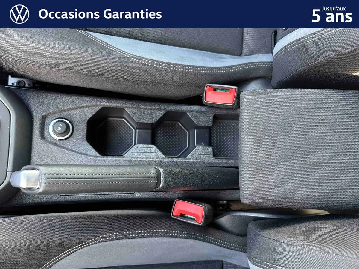 Vue plongeante sur la console centrale intérieure du Volkswagen Taigo 2025, avec frein à main manuel et sièges gris.