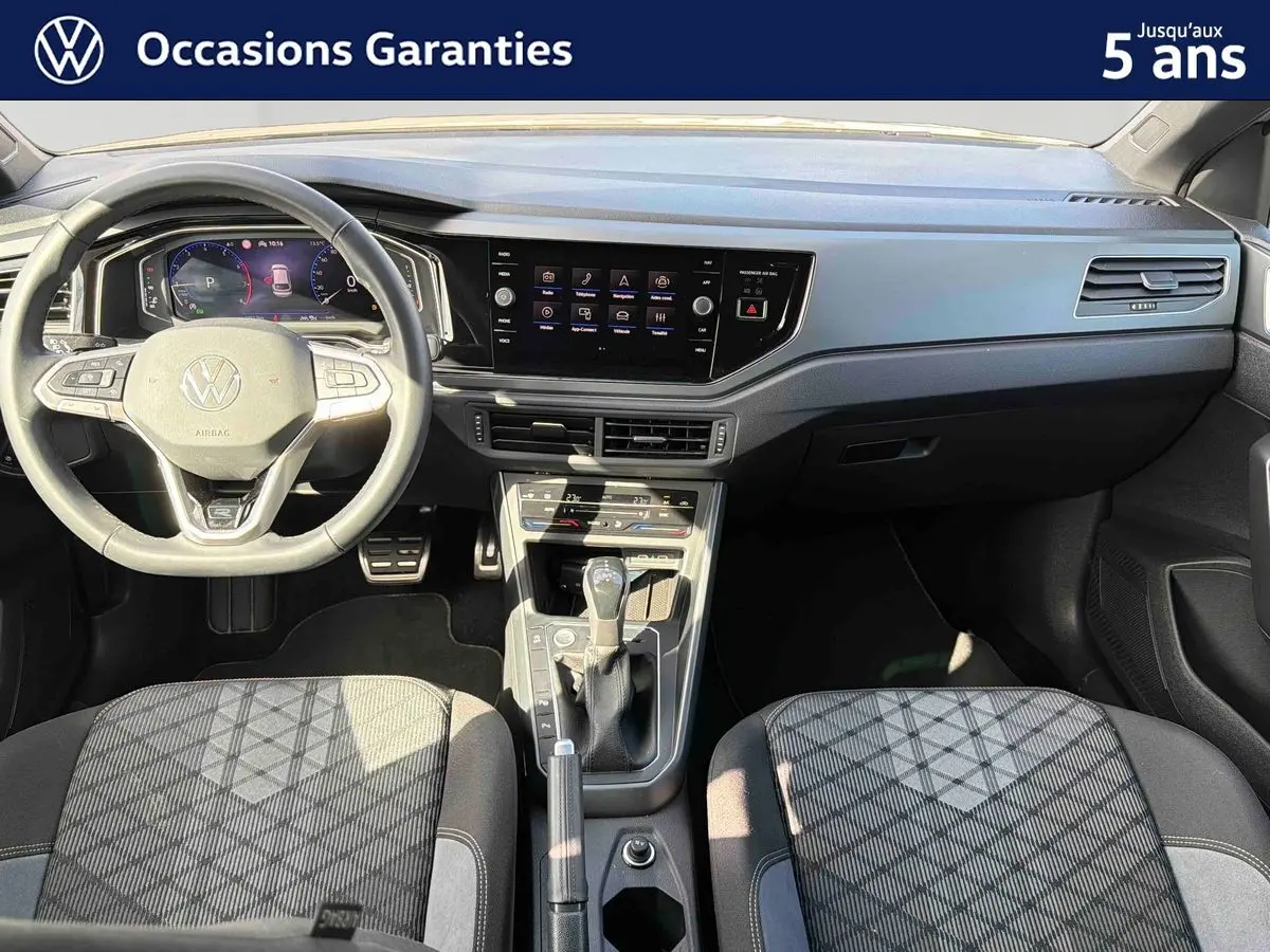 Vue intérieure avant du Volkswagen Taigo 2025, montrant le volant multifonctions, la console centrale et les sièges tissu gris à motifs.