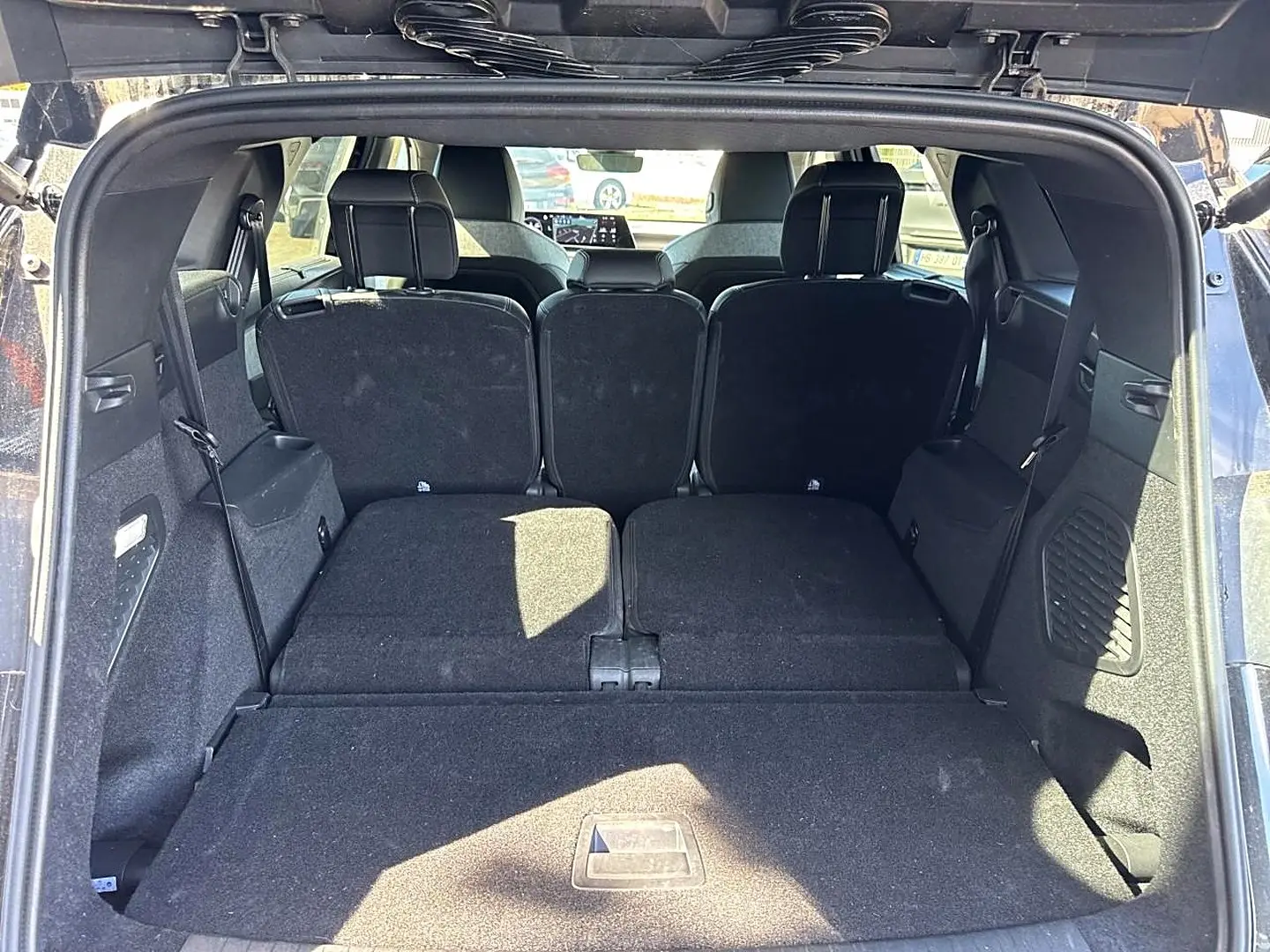 Vue depuis le coffre ouvert du Peugeot 5008 noir, montrant les sièges arrière partiellement rabattus et l'espace de chargement.