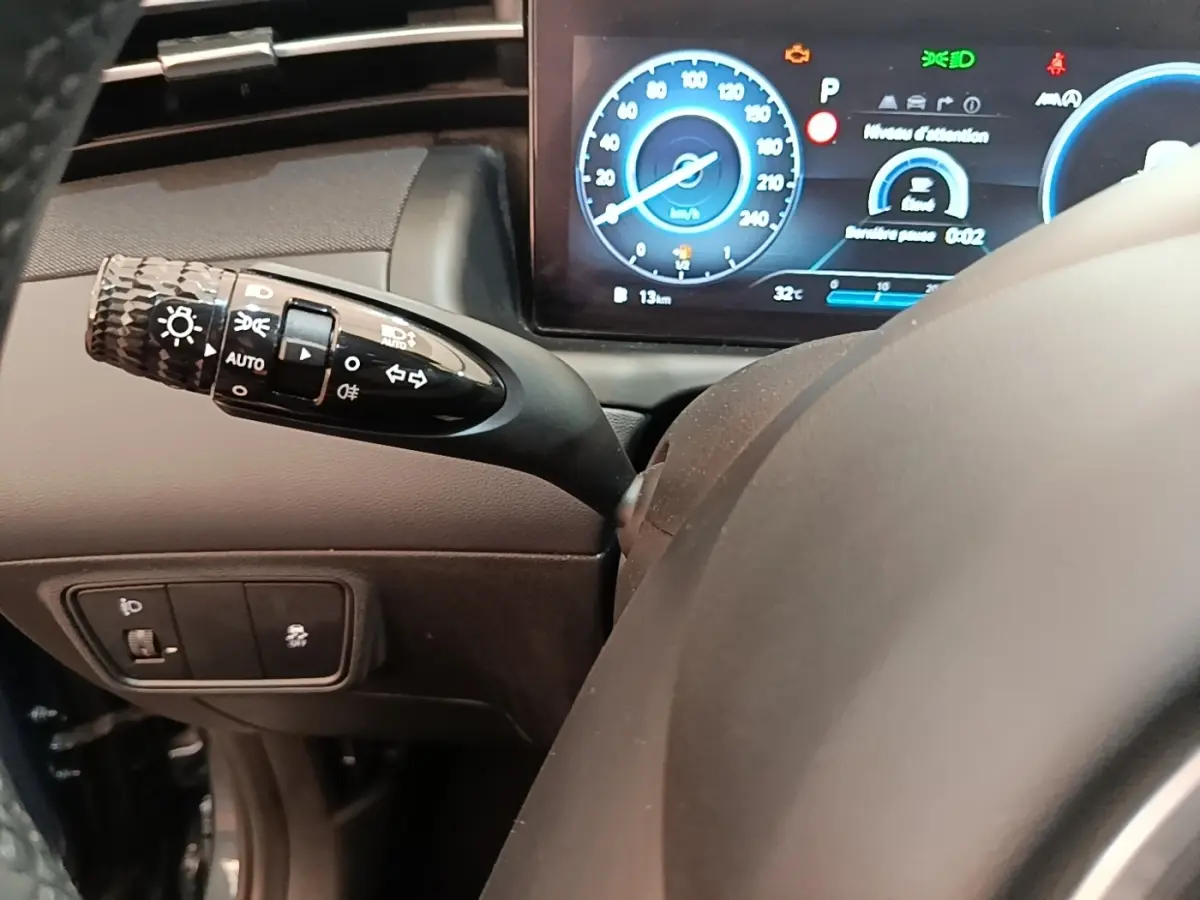 Gros plan sur le commodo des phares et clignotants à gauche du volant d’un Hyundai Tucson 2021, tableau de bord digital visible.