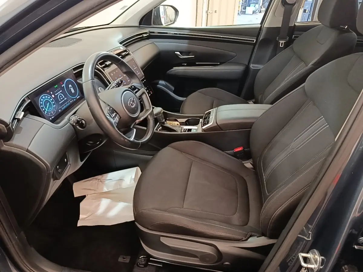 Intérieur du Hyundai Tucson 2021 vu côté conducteur, sièges noirs et tableau de bord avec écran digital.