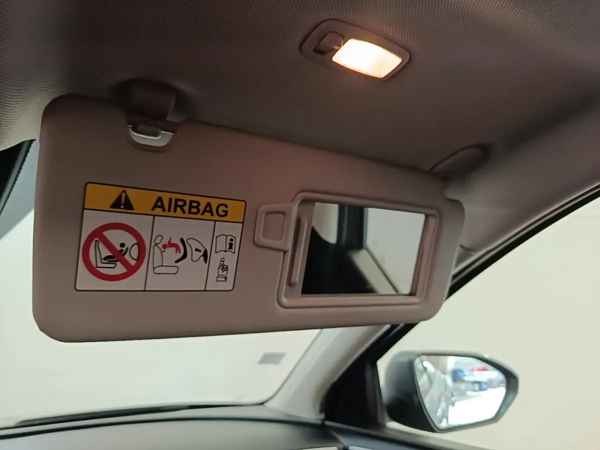 Détail intérieur du pare-soleil côté conducteur avec miroir et avertissement airbag, rétroviseur extérieur visible.
