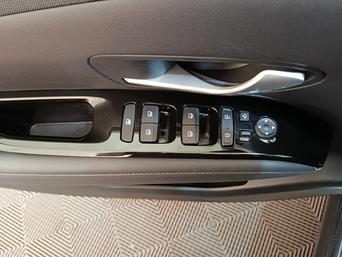 Gros plan sur la commande des vitres et rétroviseurs côté conducteur d’un Hyundai Tucson bleu, intérieur noir.