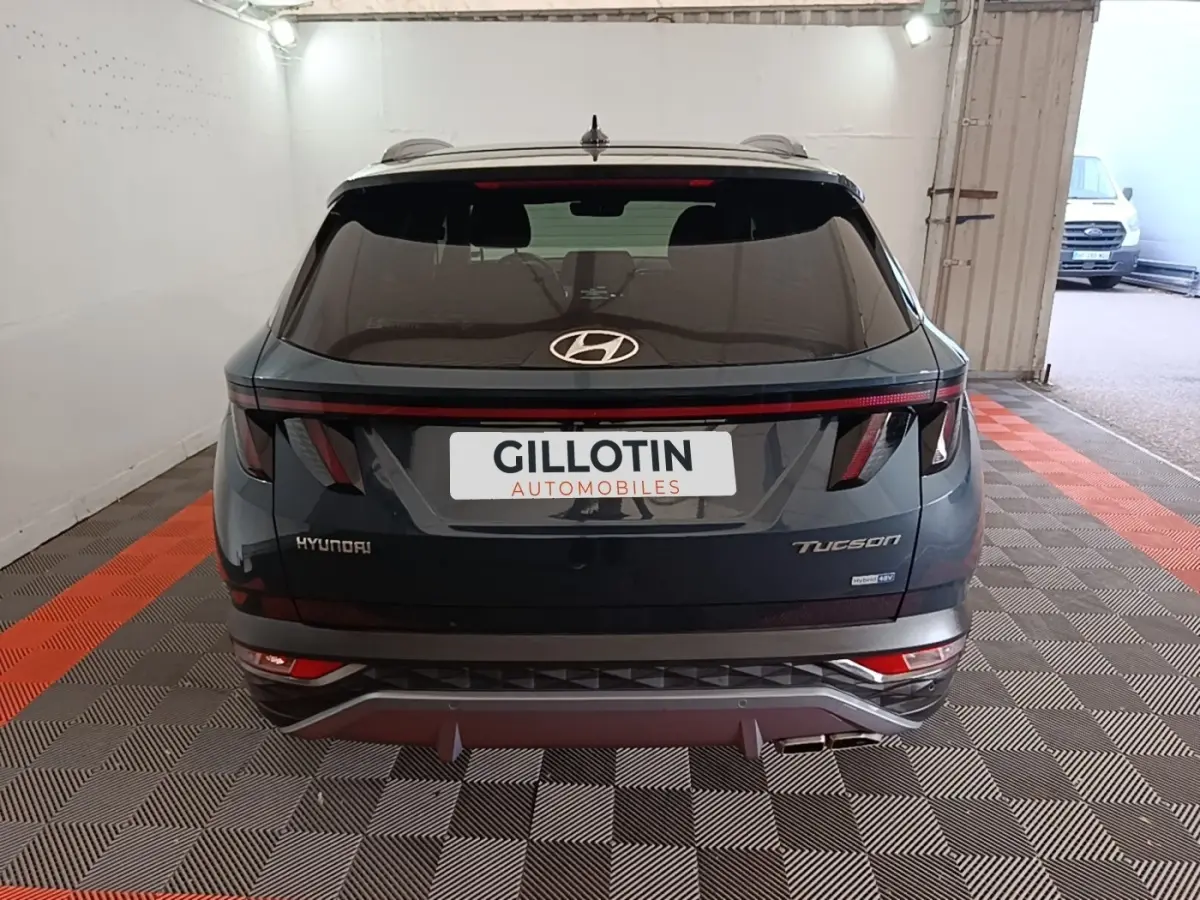 Vue arrière d’un Hyundai Tucson bleu foncé avec feux arrière en bandeau lumineux et logo Hyundai centré.