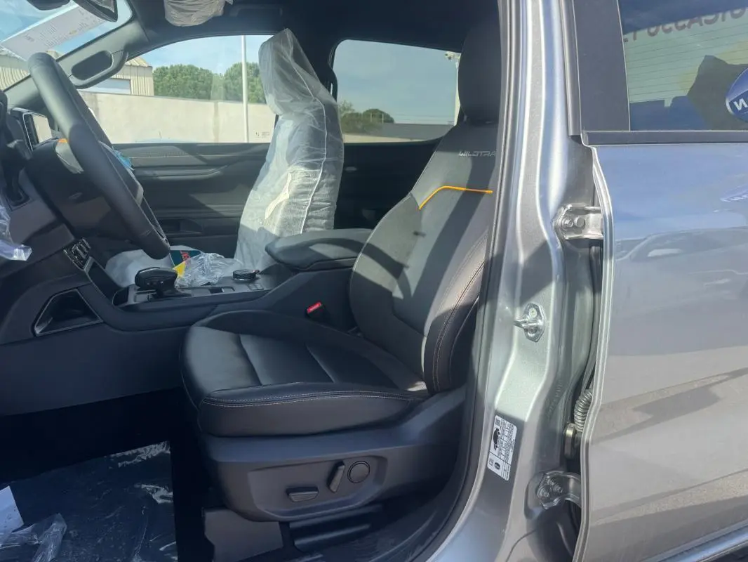 Vue côté gauche intérieur du Ford Ranger gris 2025, siège avant Wildtrak avec surpiqûres orange et accoudoir central.