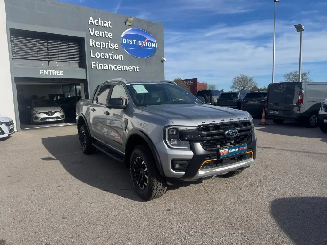 Ford Ranger Wildtrak gris en 3/4 avant droit, avec barres de toit et jantes alliage noires visibles.