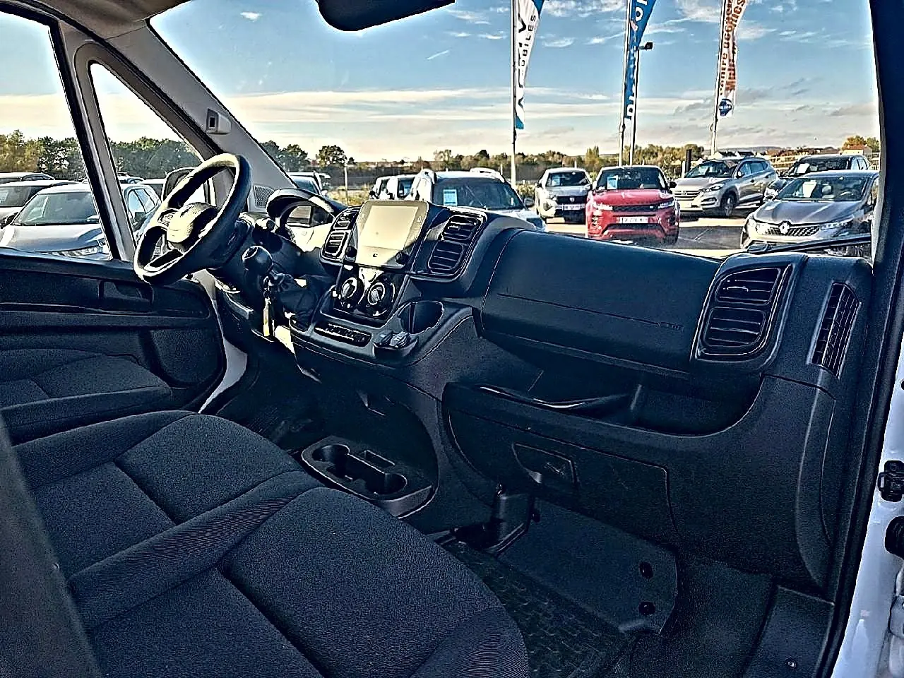 Vue intérieure côté conducteur du Peugeot Boxer Fourgon blanc, montrant le tableau de bord et la banquette avant noire.
