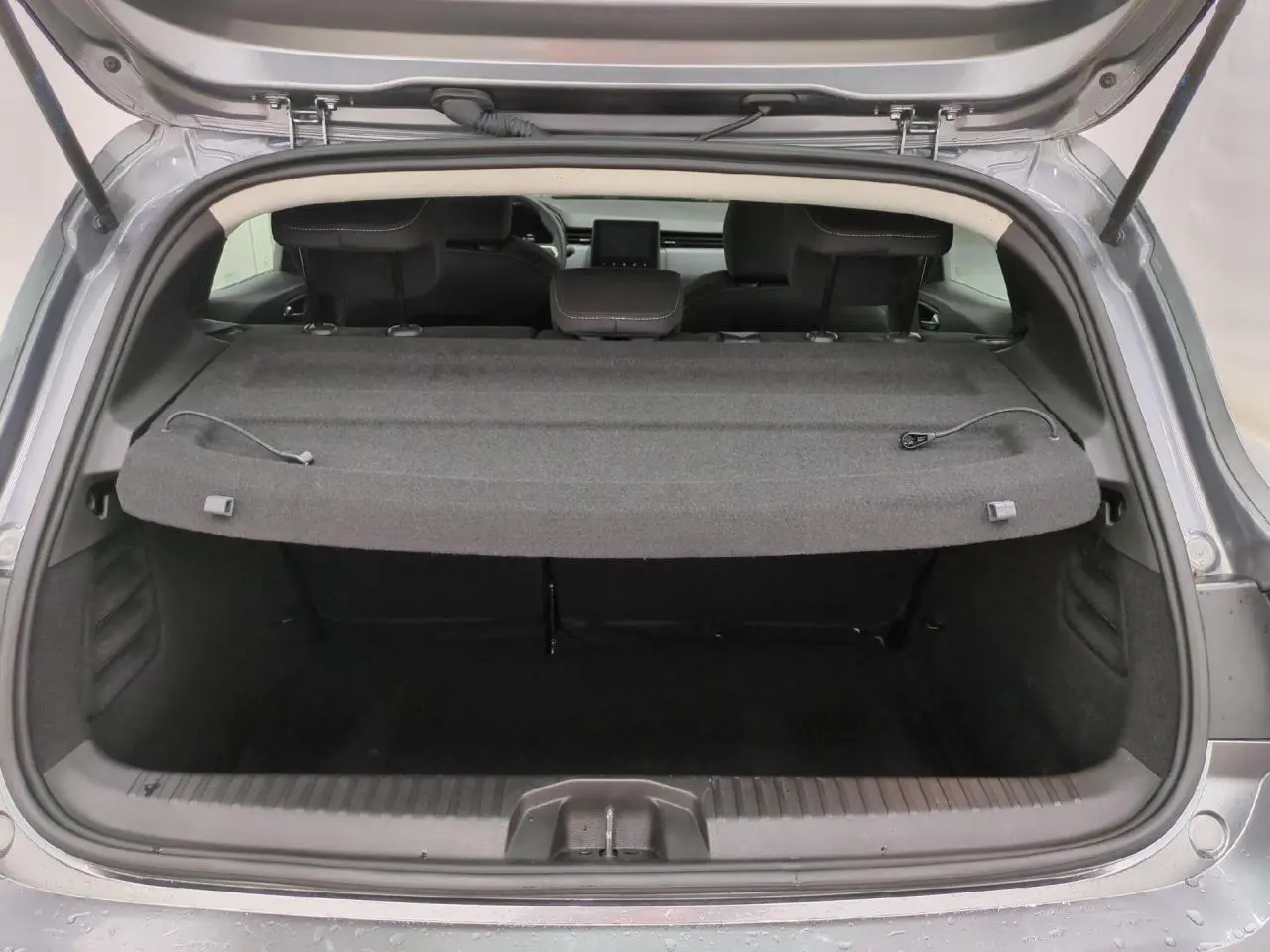 Coffre ouvert vu de l'arrière d'une Renault Clio 2024 gris foncé avec cache-bagages et sièges arrière.