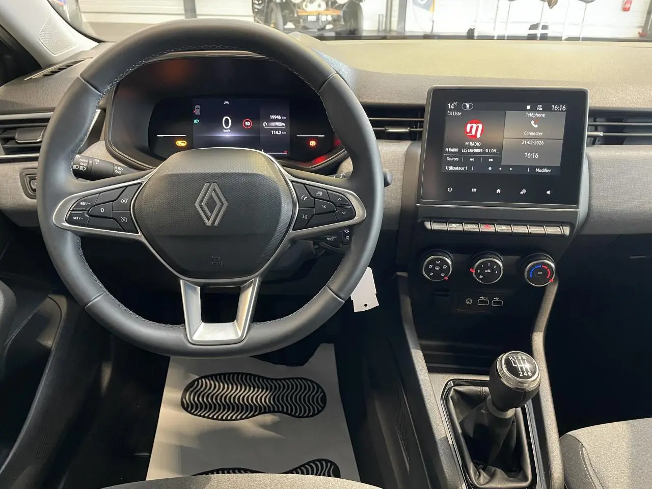 Vue intérieure centrée sur le volant et la console centrale de la Renault Clio 2024 avec levier de vitesse manuel.
