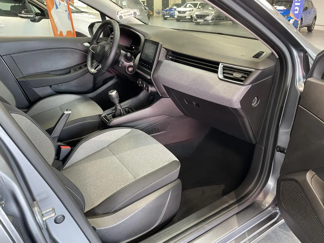 Vue intérieure côté conducteur de la Renault Clio gris foncé 2024 avec sellerie tissu gris et tableau de bord moderne.