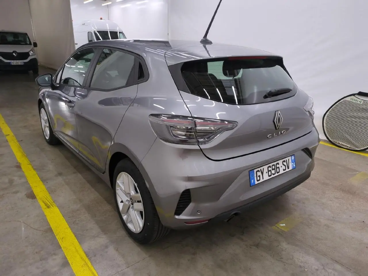 Renault Clio gris foncé vue 3/4 arrière droit, avec feux LED et jantes alliage 16 pouces en intérieur garage.