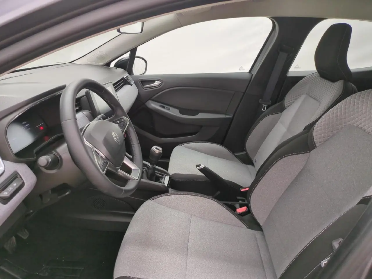 Vue intérieure côté conducteur de la Renault Clio 2024, sièges tissu gris et volant multifonction noir.