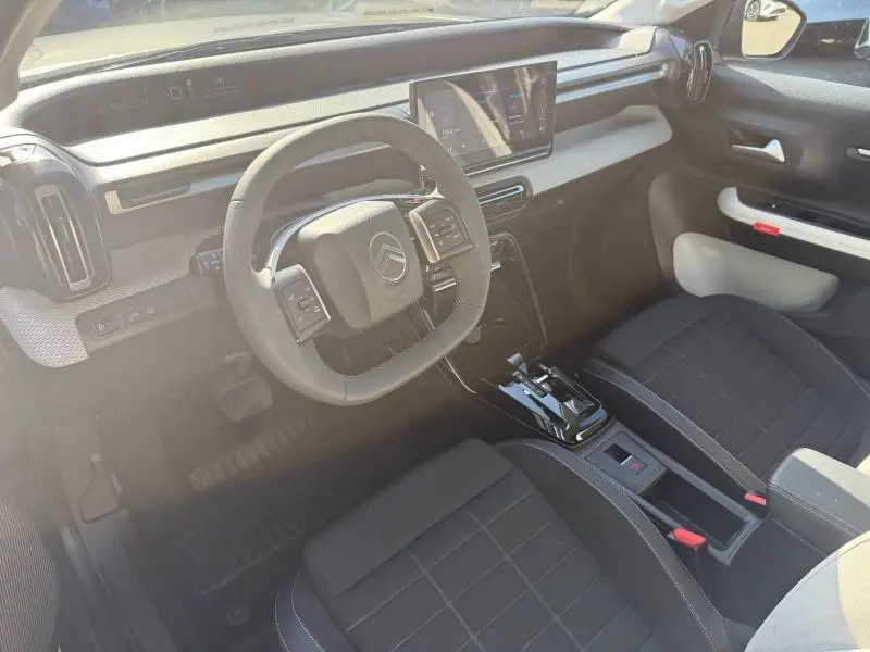 Intérieur de la Citroën C3 électrique 2025 vu côté conducteur, avec tableau de bord noir et sièges tissu noir.