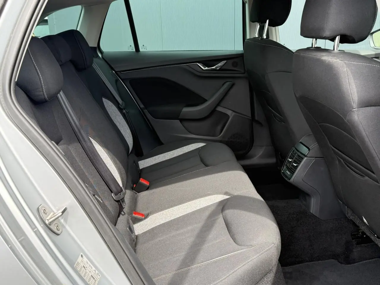 Vue intérieure côté arrière gauche de la Skoda Scala TSI 116 DSG7 Sélection, sièges tissu gris et noir.
