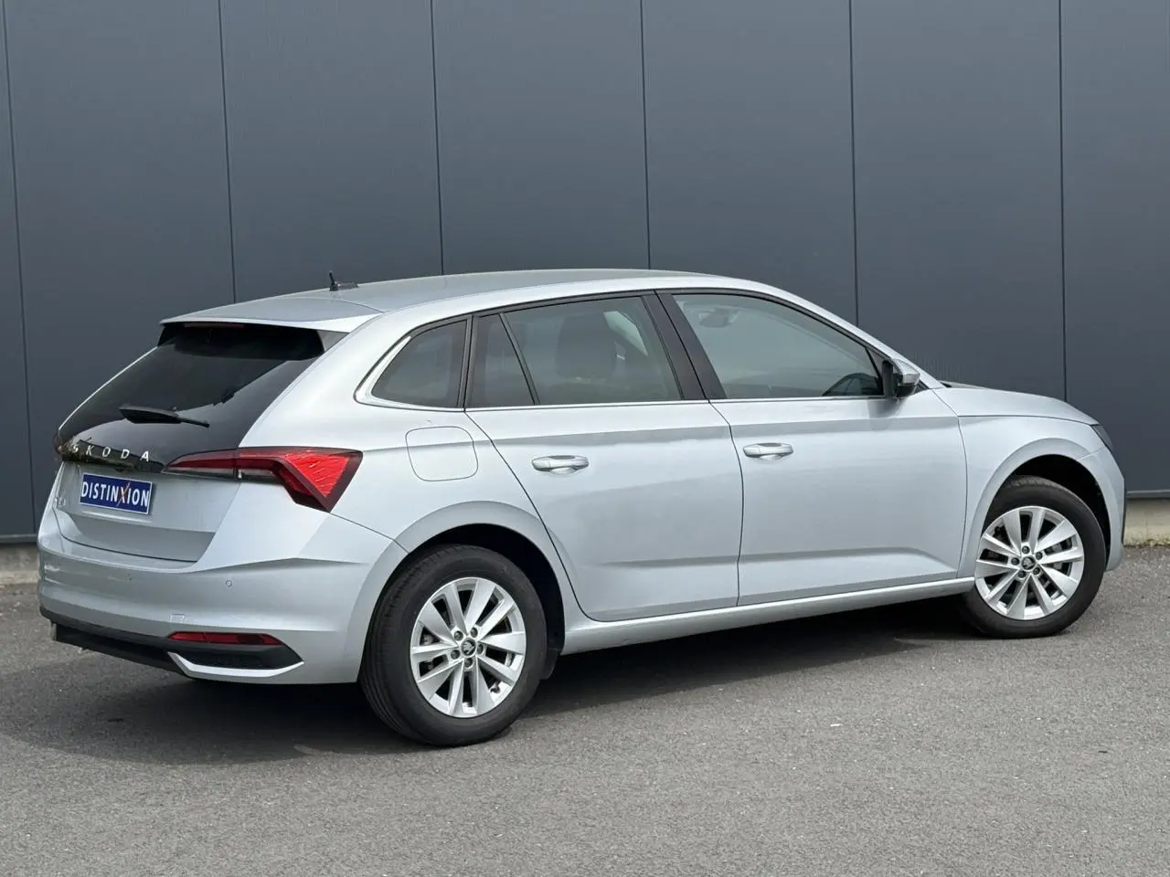 Vue 3/4 arrière droite d'une Skoda Scala gris Reflex avec vitres arrière surteintées et jantes alliage 16 pouces.
