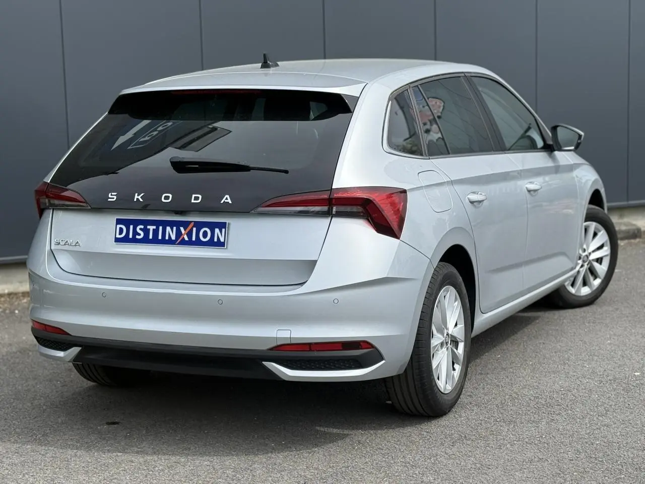 Vue 3/4 arrière droite d'une Skoda Scala TSI 116 DSG7 gris reflex avec vitres surteintées et jantes alliage 16 pouces.