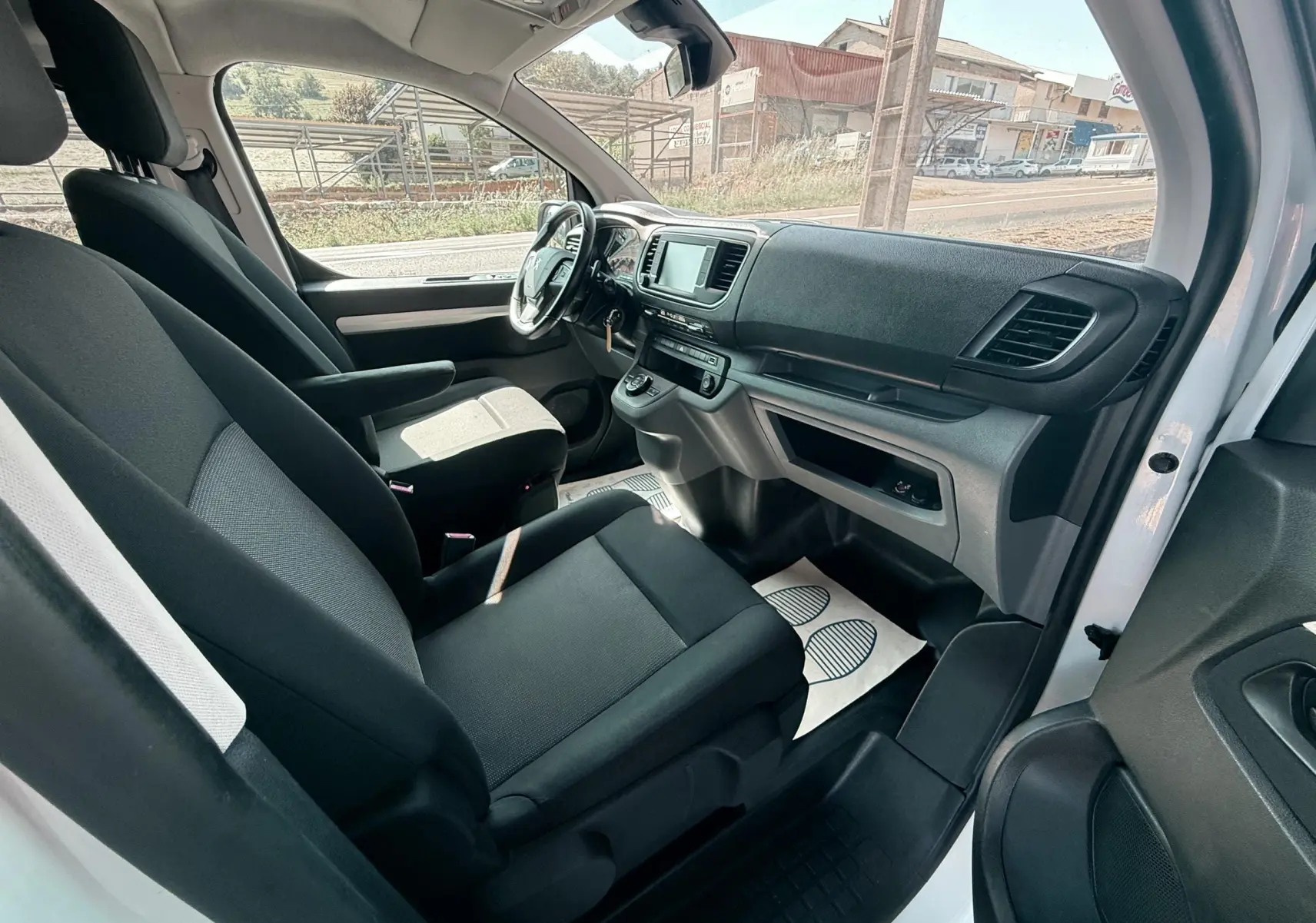 Vue intérieure côté conducteur du Peugeot Expert cabine approfondie blanc, montrant les sièges tissu gris noir et le tableau de bord moderne.