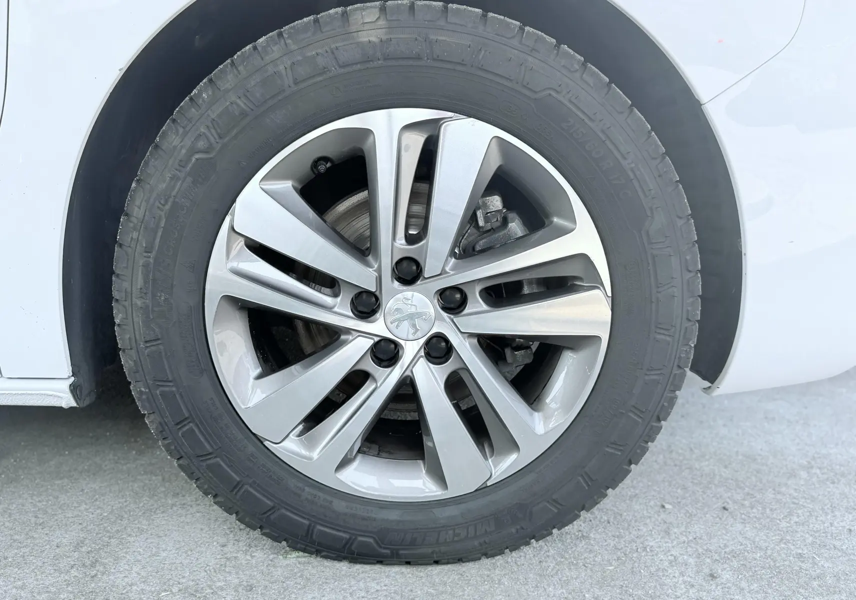Gros plan sur la roue avant droite d’un Peugeot Expert blanc, jante alliage argentée avec logo lion au centre.