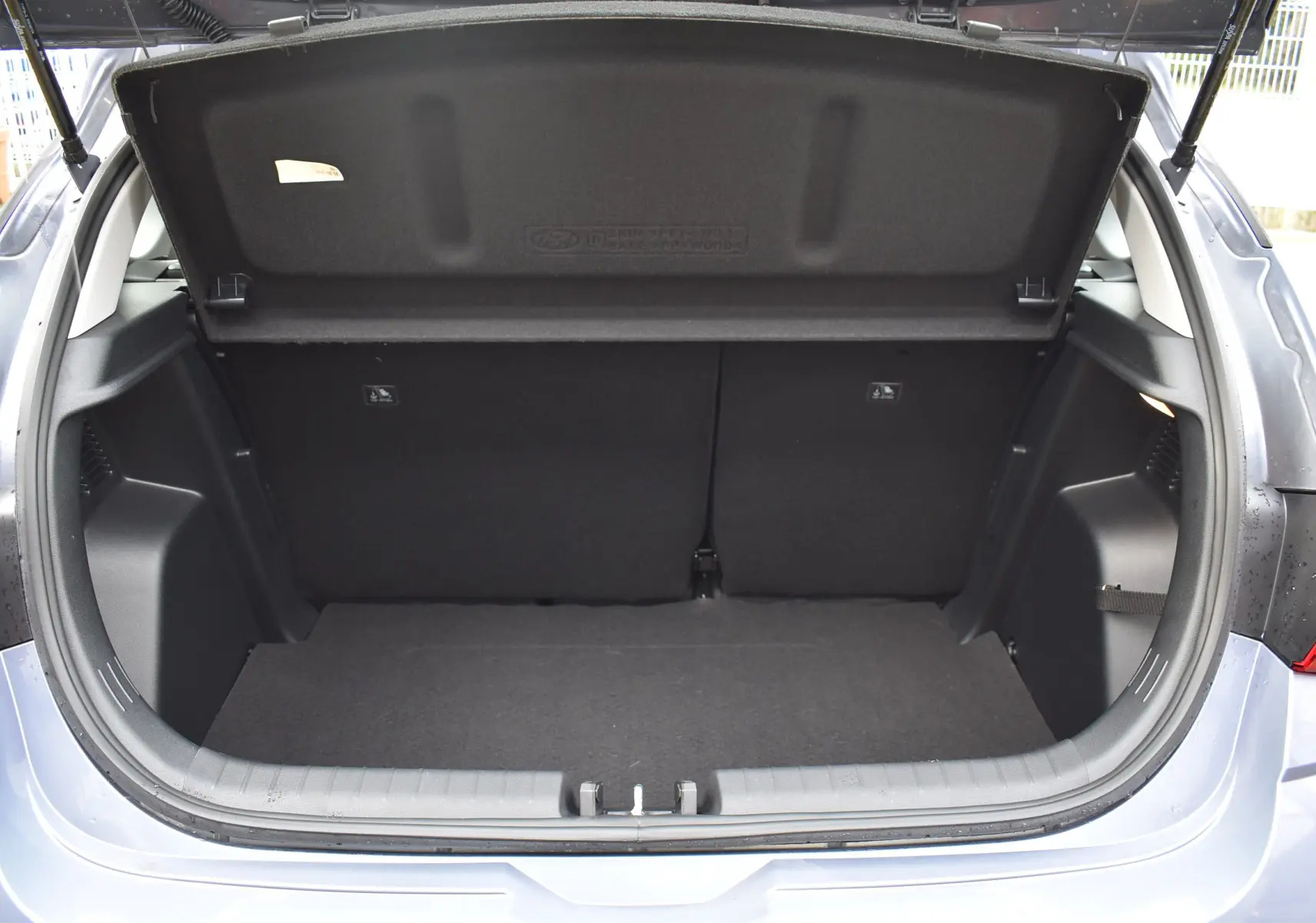 Coffre ouvert d'une Hyundai i20 bleu clair vue arrière, avec cache-bagages rigide et intérieur noir.