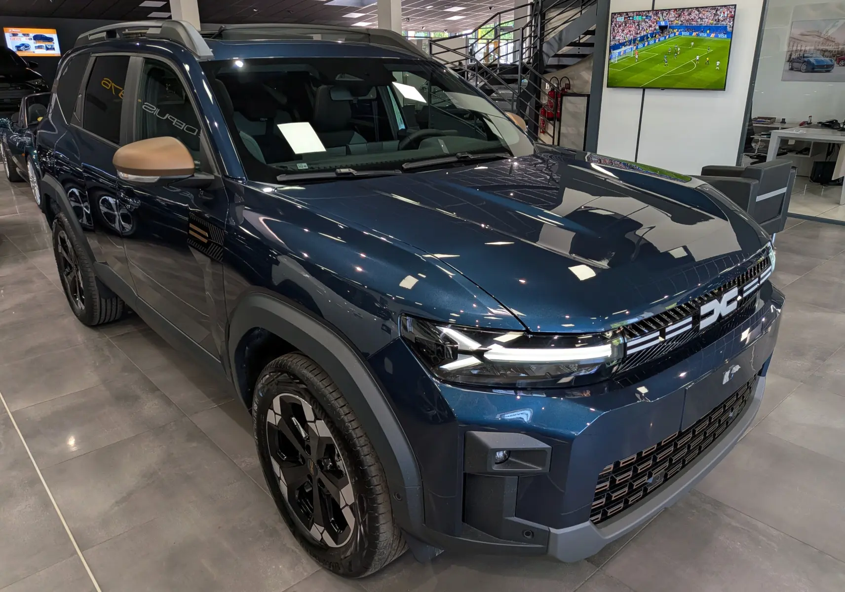 Vue 3/4 avant gauche du Dacia Bigster bleu indigo avec rétroviseurs couleur bronze en showroom.